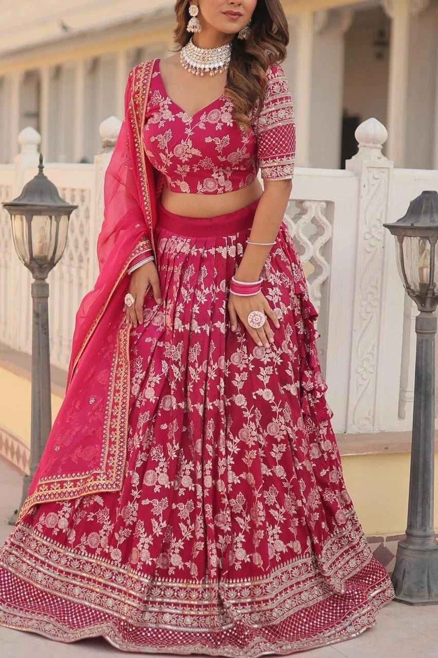 Woman wearing a pink embroidered traditional outfit with jewelry in an outdoor setting.